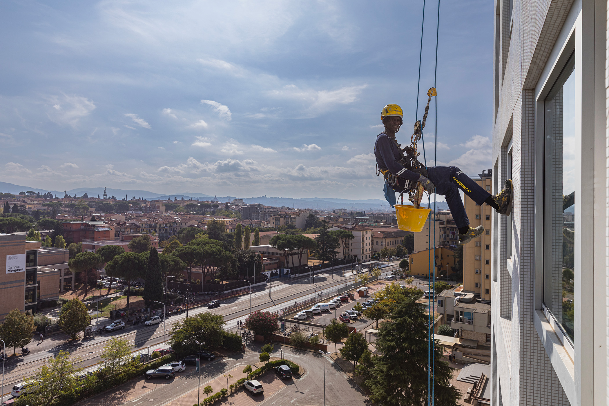 Operatore su fune sospeso mentre esegue una manutenzione sulla facciata di un edificio alto