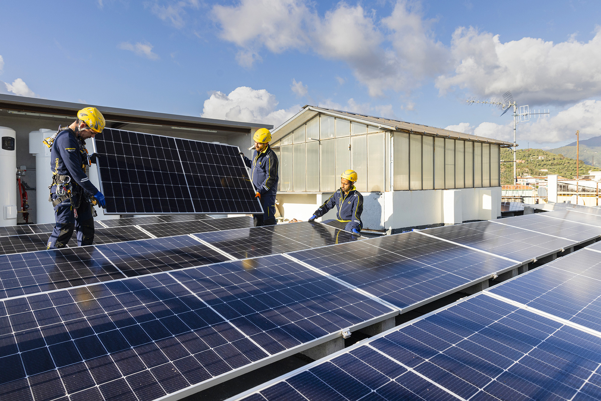 Tecnici Acrobatica Energy con il casco giallo installano pannelli fotovoltaici su un tetto