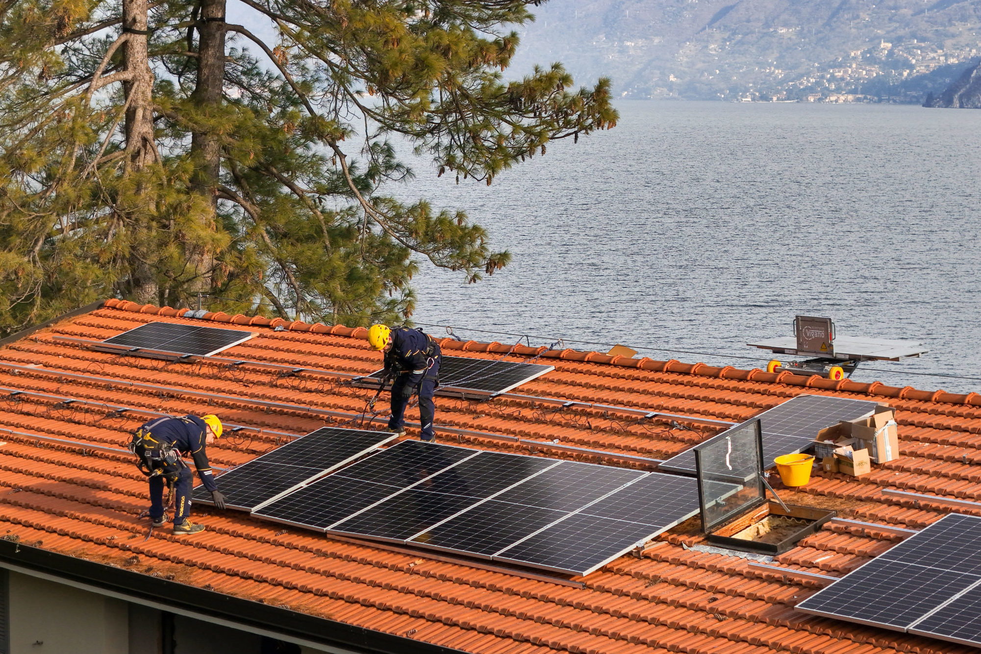 Due tecnici installano pannelli fotovoltaici su un tetto in coppi affacciato sul lago