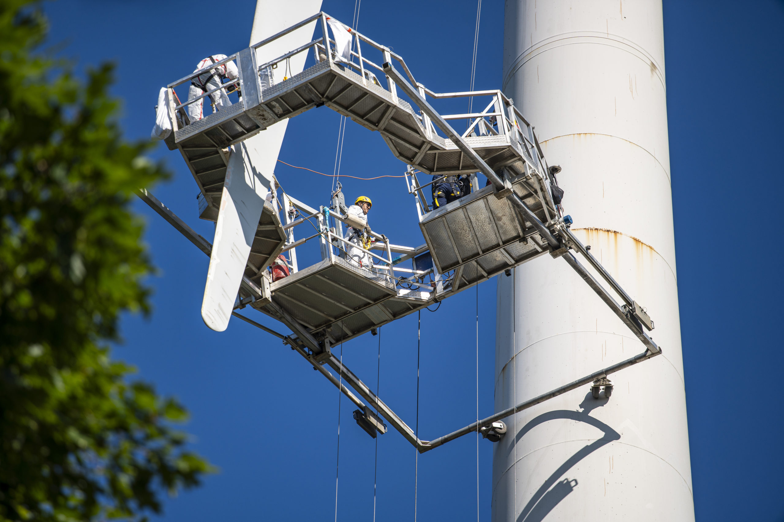 Piattaforma sospesa attorno alla pala di un aerogeneratore, con gli operatori al lavoro