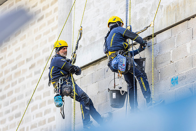 Due operatori su fune Acrobatica con il casco giallo al lavoro su un edificio in cemento