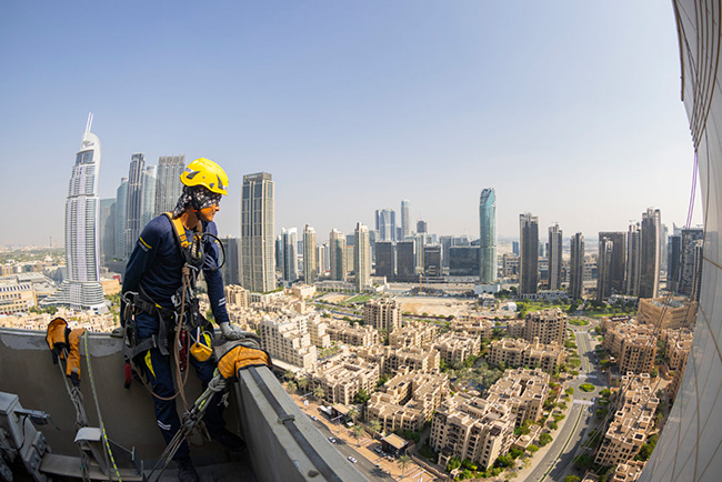 Operatore su fune con imbracatura su un grattacielo affacciato sullo skyline di Dubai